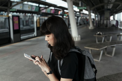 Full length of woman using mobile phone at bus