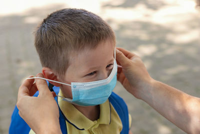 Dad puts on or adjusts a protective mask in front of school or kindergarten for his son. 