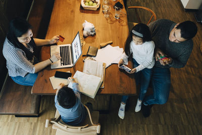 High angle view of mother using laptop at table while father sitting with children in living room