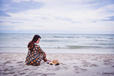 Woman sitting at beach against sky