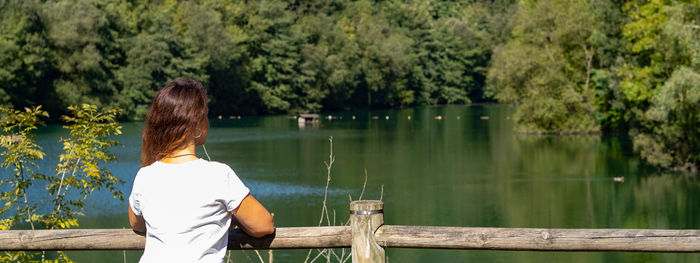 Rear view of woman looking at lake against trees