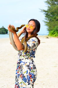 Young woman holding snake while standing on sand at beach