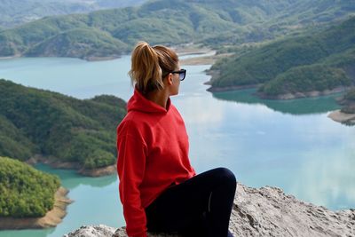 Woman sitting on mountain by lake against mountains