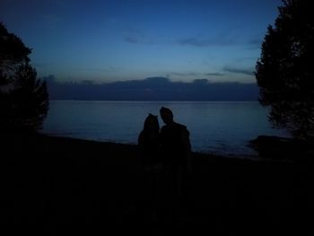 Silhouette man sitting by sea against sky during sunset