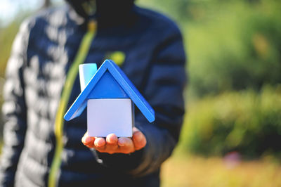 Midsection of man holding toy blocks forming model home