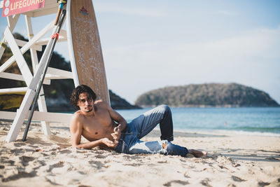 Full length of shirtless man sitting on beach