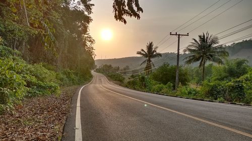 Road amidst trees against sky during sunset