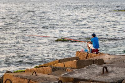 Man fishing on rock by sea
