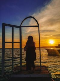 Rear view of woman looking at sea against sunset sky