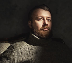 Portrait of serious mature man sitting on chair in darkroom at home