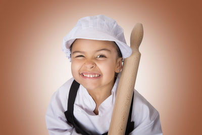 Portrait of girl in chef uniform holding rolling pin against orange background