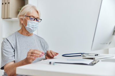 Senior woman wearing mask sitting at hospital