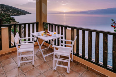 Chairs and table at balcony against sky during sunset