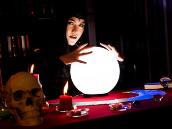 Portrait of woman sitting by illuminated lantern on table