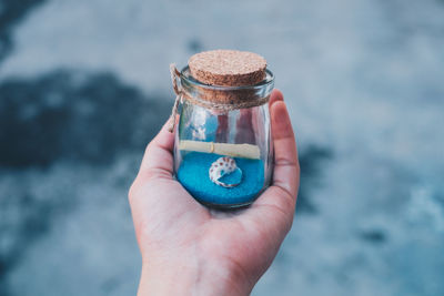 Cropped hand holding note and seashell in jar