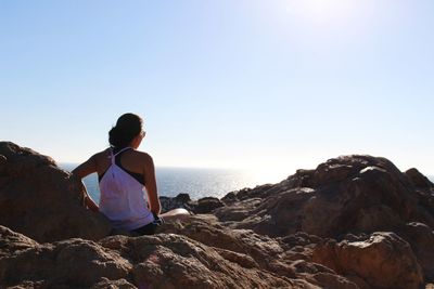 Rear view of woman standing on rock by sea against clear sky