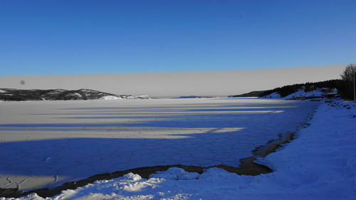 Scenic view of frozen lake against clear blue sky