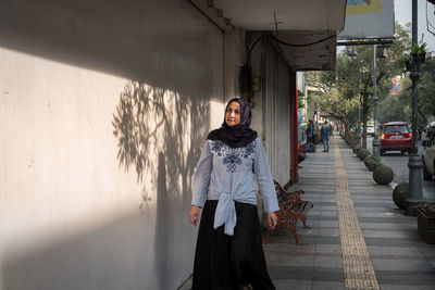 Portrait of smiling young woman standing against building