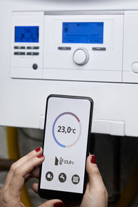 Woman adjusting temperature of heating boiler through mobile phone at home