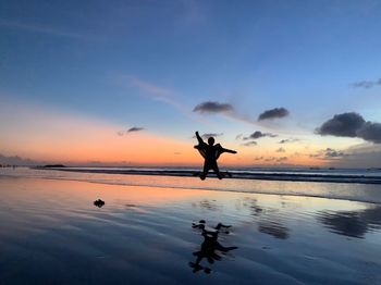 Silhouette woman jumping at beach against sky during sunset