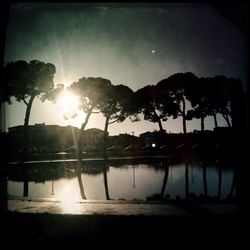 Silhouette trees by lake against sky during sunset