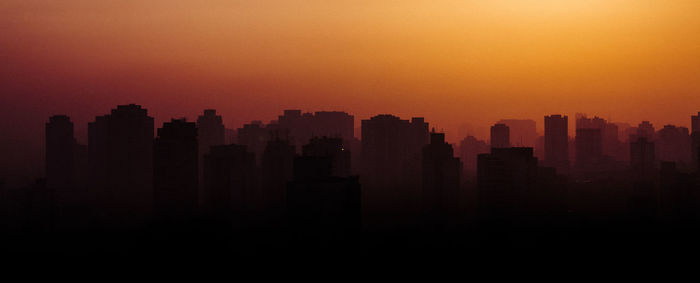 Silhouette buildings in city against sky during sunset