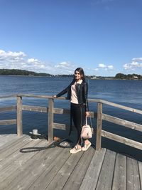 Full length of woman sitting on wood by sea against sky