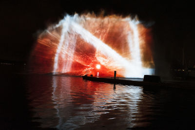 Illuminated fountain in lake against sky at night