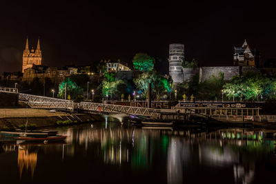Illuminated bridge over river against buildings in city at night