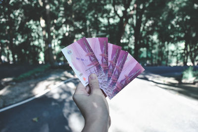 Low angle view of hand holding paper against tree