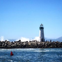 Lighthouse by sea against clear sky