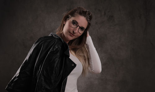 Portrait of young woman standing against black background