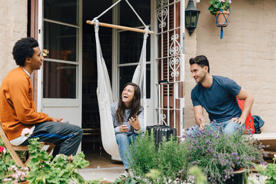 Smiling friends talking while sitting by plants against home