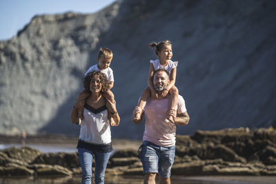 Parents carrying children on shoulder while walking at beach