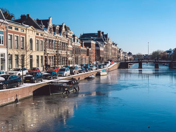 Boats moored in canal by buildings against clear blue sky