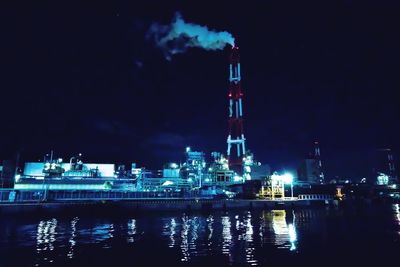 Illuminated factory by river against sky at night