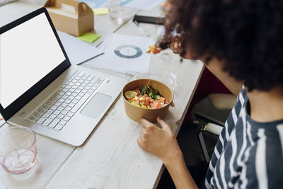 Businesswoman having poke bowl by laptop in lunch break at office