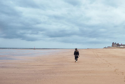 Rear view of woman walking on beach against sky