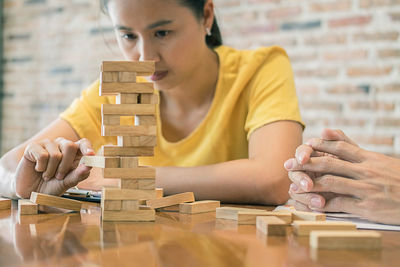 Cropped hands of man by friend stacking wooden blocks on table