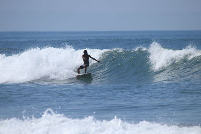 Man surfing on waves in sea against sky