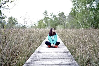 Full length of woman sitting on grass against trees