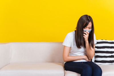 Woman wearing mask sitting on sofa at home