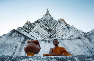 Low angle view of man sitting outside building against sky