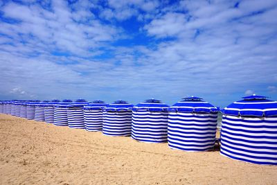 Row of deck chairs on beach against blue sky