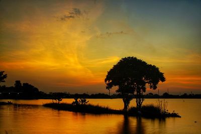 Silhouette trees by lake against romantic sky at sunset