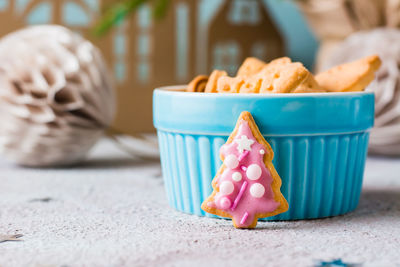 Christmas cookies spruce with pink icing are placed near a bowl of cookies on a decorated table