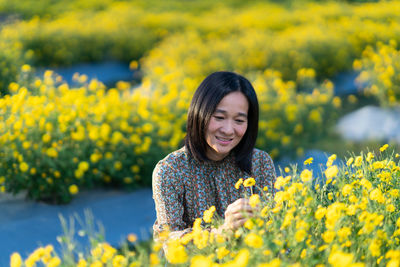 Portrait of smiling young woman with yellow flower on field