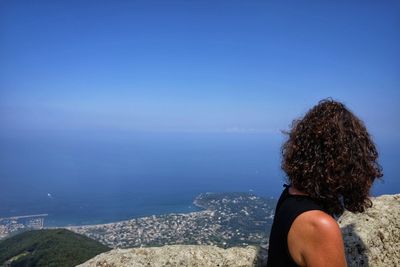 Side view of woman looking at sea against blue sky