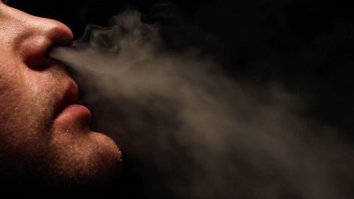 Cropped image of man smoking against black background