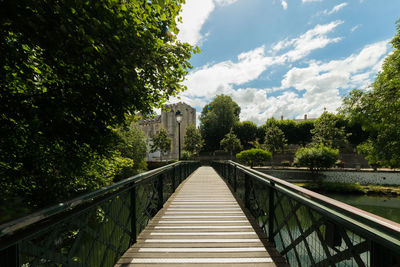 Footbridge amidst trees against sky